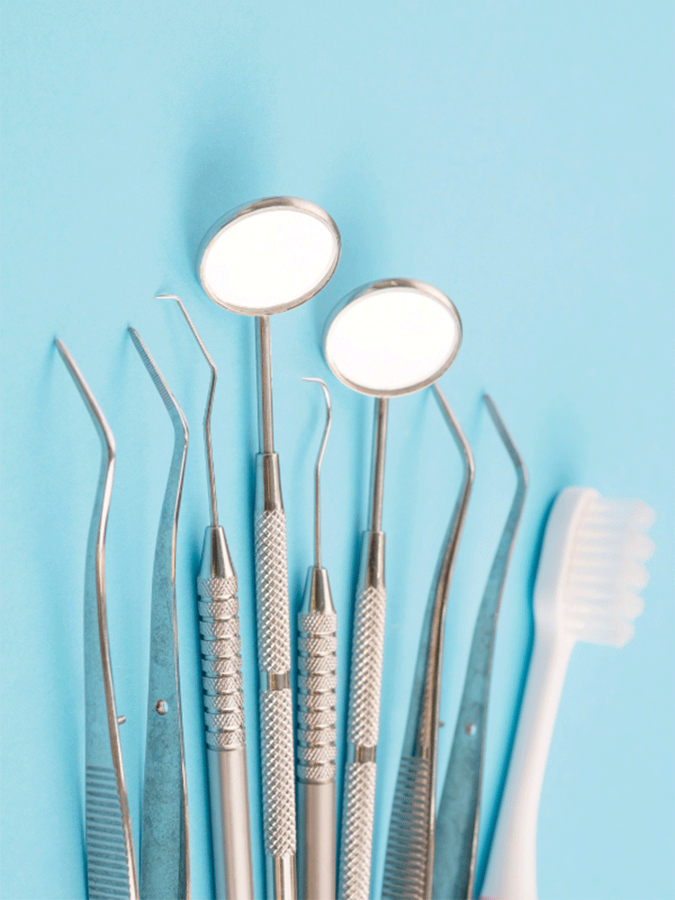 Collection of dental tools on a light blue background, including mirrors, probes, tweezers, and a toothbrush—essentials for dental care and hygiene.