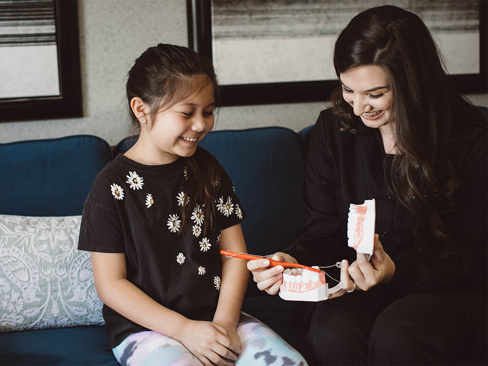 dental hygienist demonstrating to a little girl how to brush her teeth
