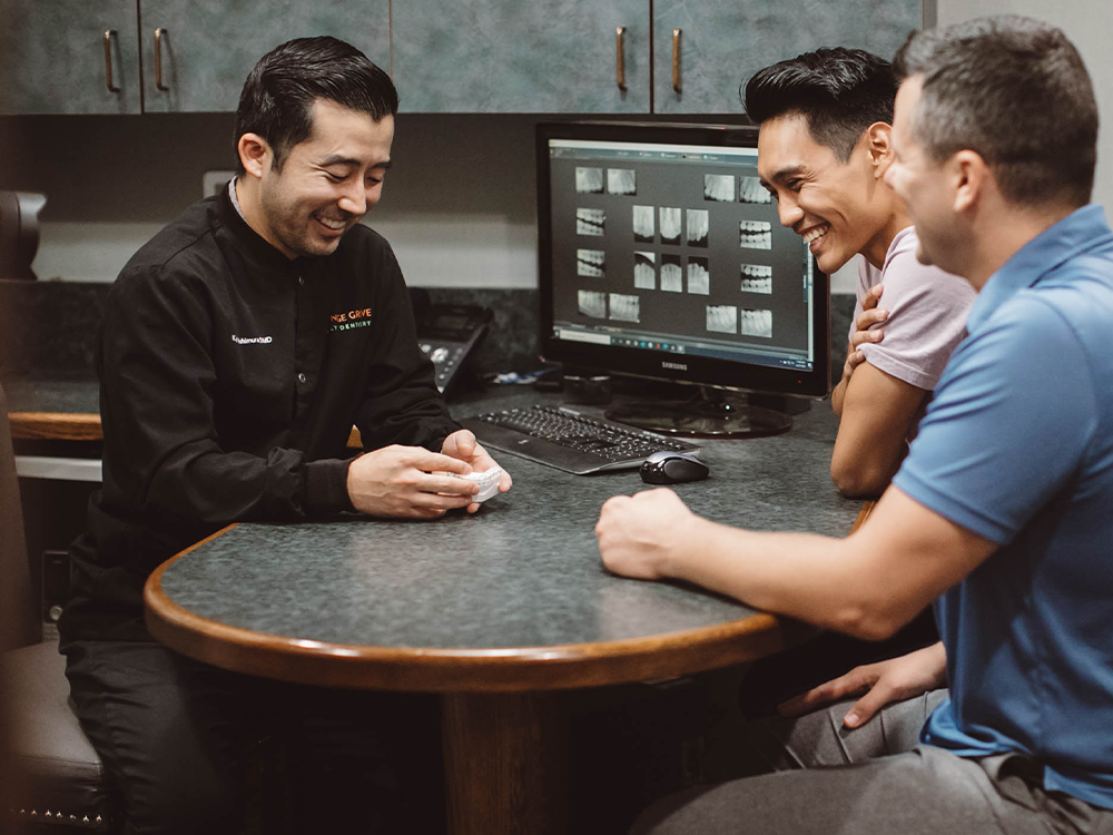 dr nishimura talking to dental patients holding a fake pair of teeth