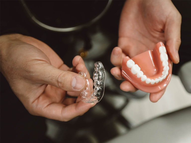 image of a person holding an invisalign tray and a pair of fake teeth